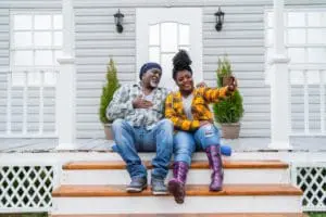 A couple sits on the steps and takes a picture in front of their home