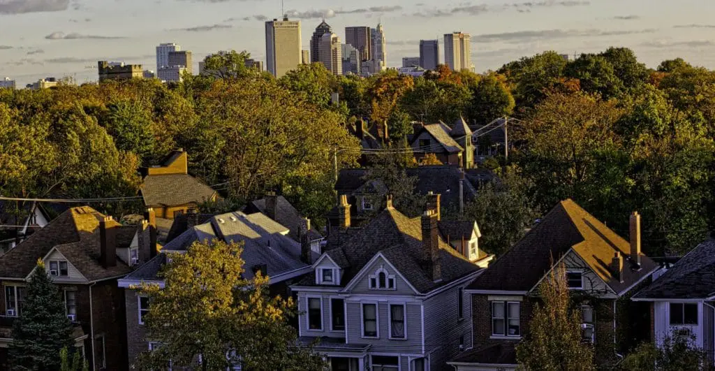 An image of a house in a neighborhood with trees and a city skyline in the background