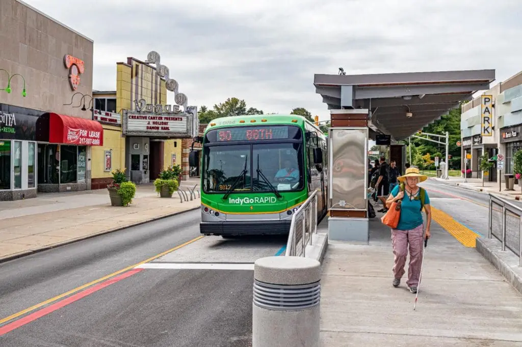 A bus uses a bus lane as a blind woman walks away from a protected bus shelter