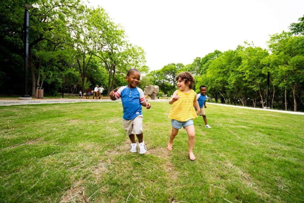 Two toddler-age children run through a large greenspace