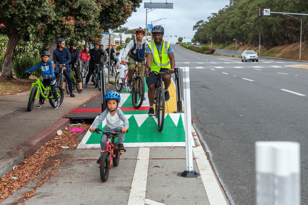A group of bicyclists of different ages use a protected bike lane